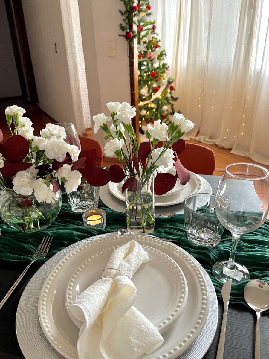 Mesa navideña con camino verde, claveles blancos y hojas de eucalipto rojo